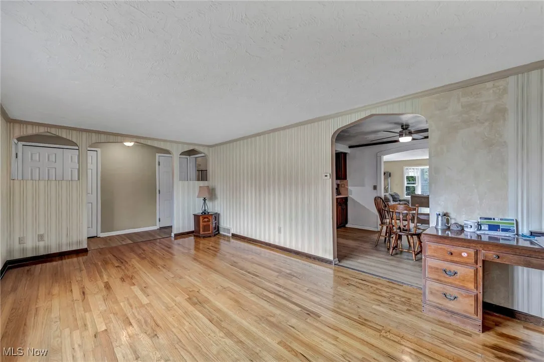 Living area featuring crown molding, arched walkways, light wood finished floors, and a textured ceiling