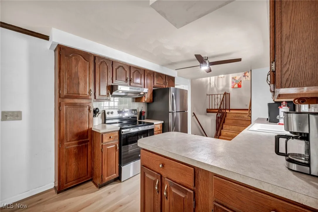 Kitchen featuring backsplash, light wood-type flooring, light countertops, under cabinet range hood, and stainless steel appliances