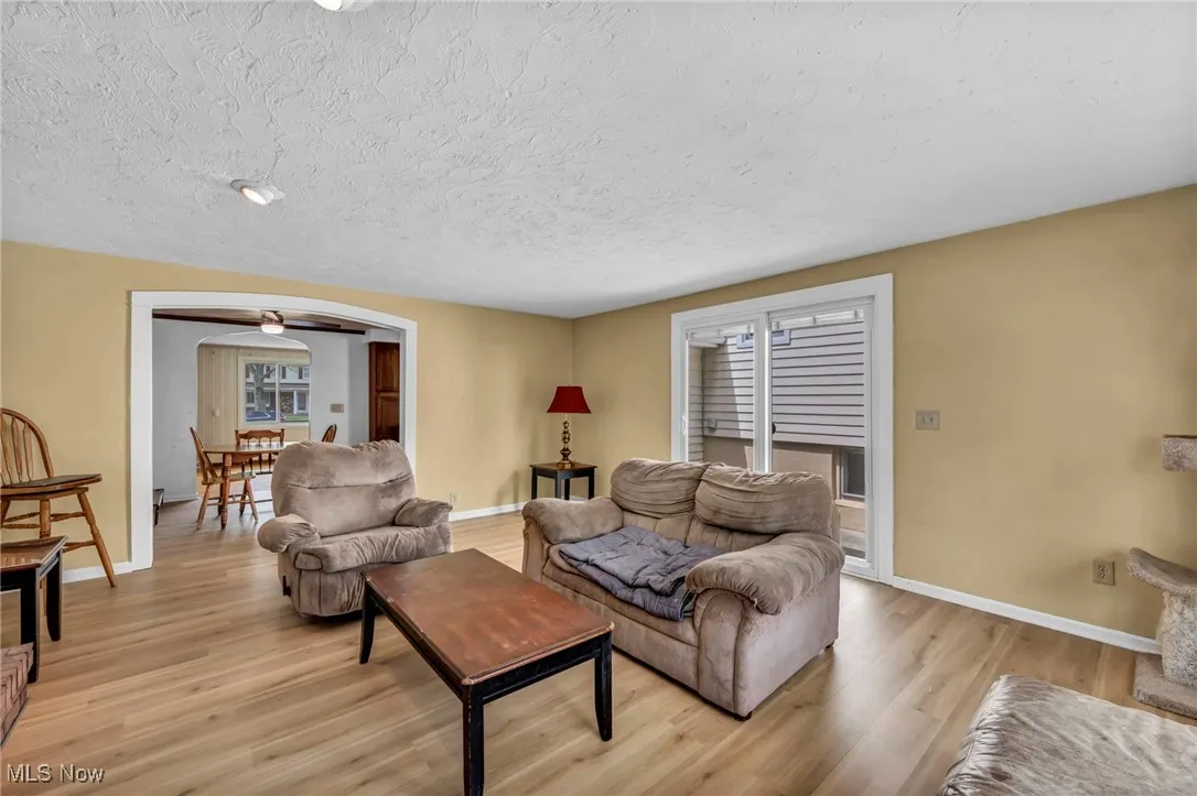 Living room with a textured ceiling, baseboards, arched walkways, and light wood finished floors