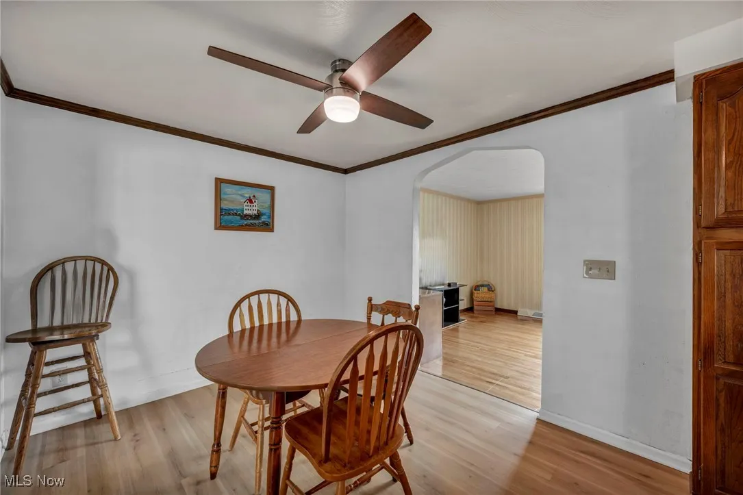Dining room featuring a ceiling fan, ornamental molding, baseboards, light wood-type flooring, and arched walkways