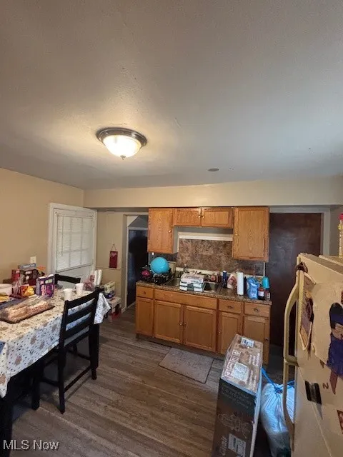 Kitchen with brown cabinetry, dark wood finished floors, backsplash, and fridge