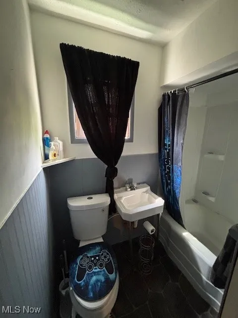 Full bathroom with toilet, wainscoting, a sink, and shower / bath combo with shower curtain