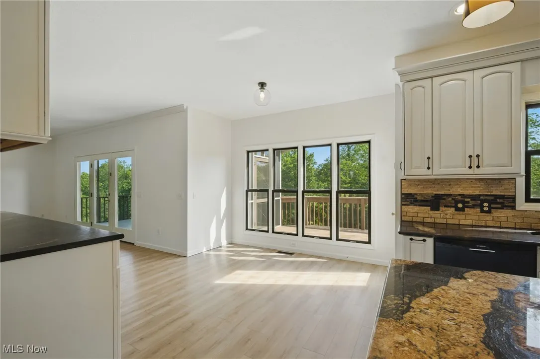 Kitchen with light wood finished floors, ornamental molding, tasteful backsplash, and dark stone counters