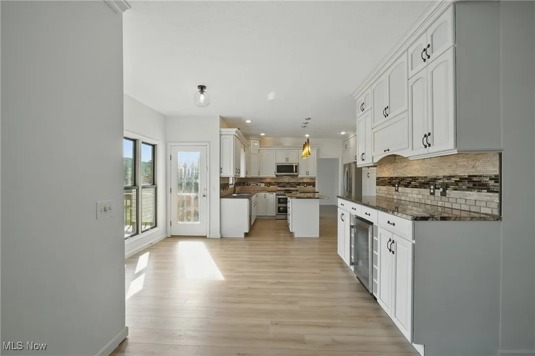 Kitchen featuring stainless steel appliances, wine cooler, tasteful backsplash, white cabinetry, and light wood-style floors