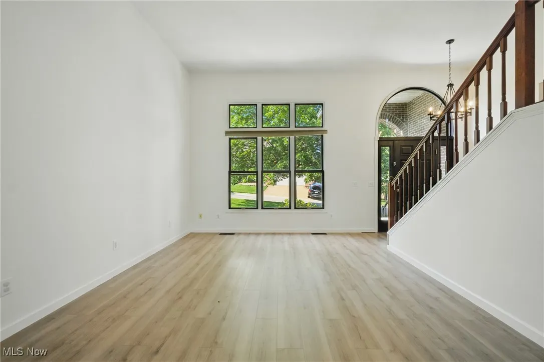 Unfurnished living room with light wood-style floors, a chandelier, and stairway