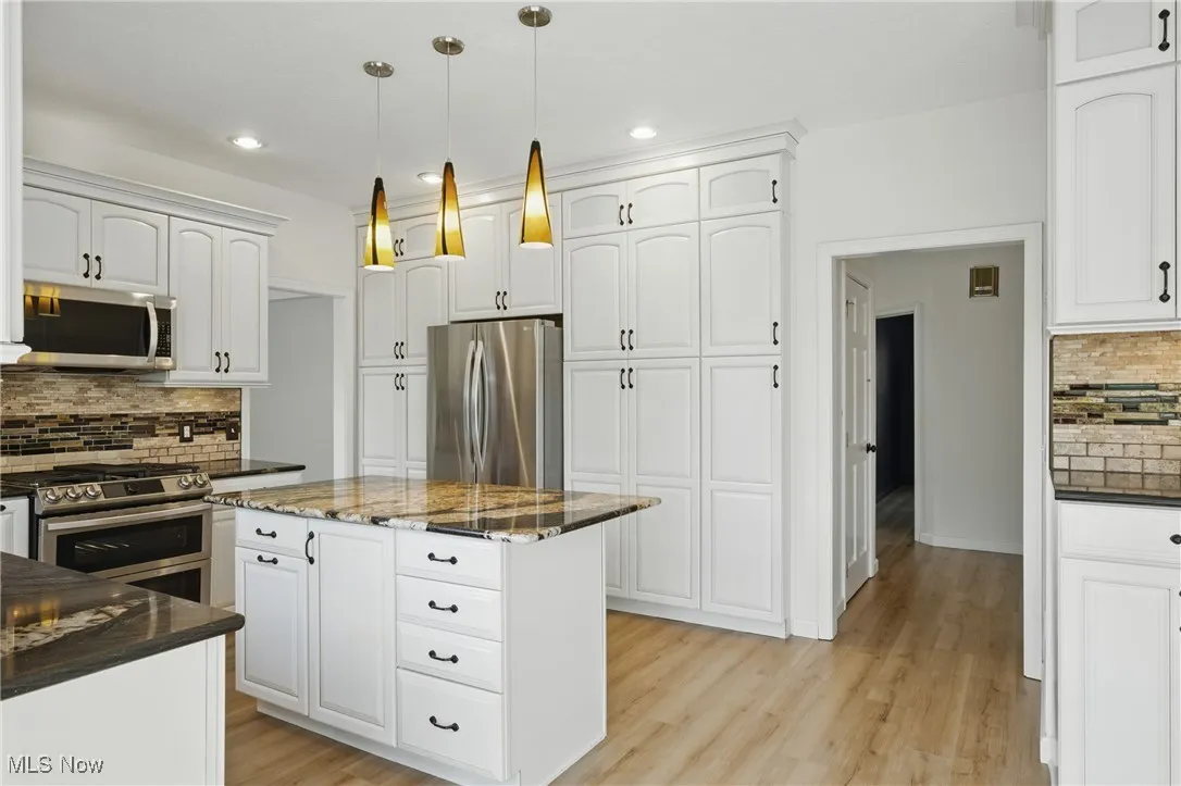Kitchen featuring stainless steel appliances, tasteful backsplash, dark stone counters, light wood-style floors, and white cabinets