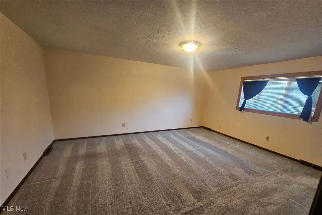 Unfurnished room with a textured ceiling, baseboards, and carpet