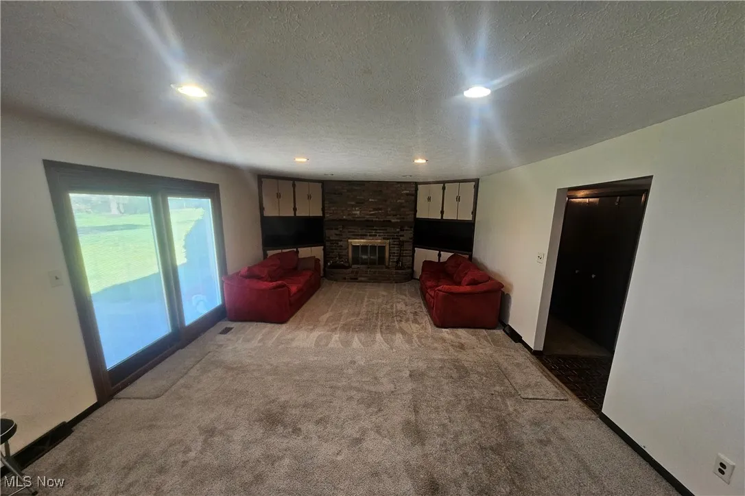 Living area featuring a textured ceiling, a fireplace, baseboards, light carpet, and recessed lighting
