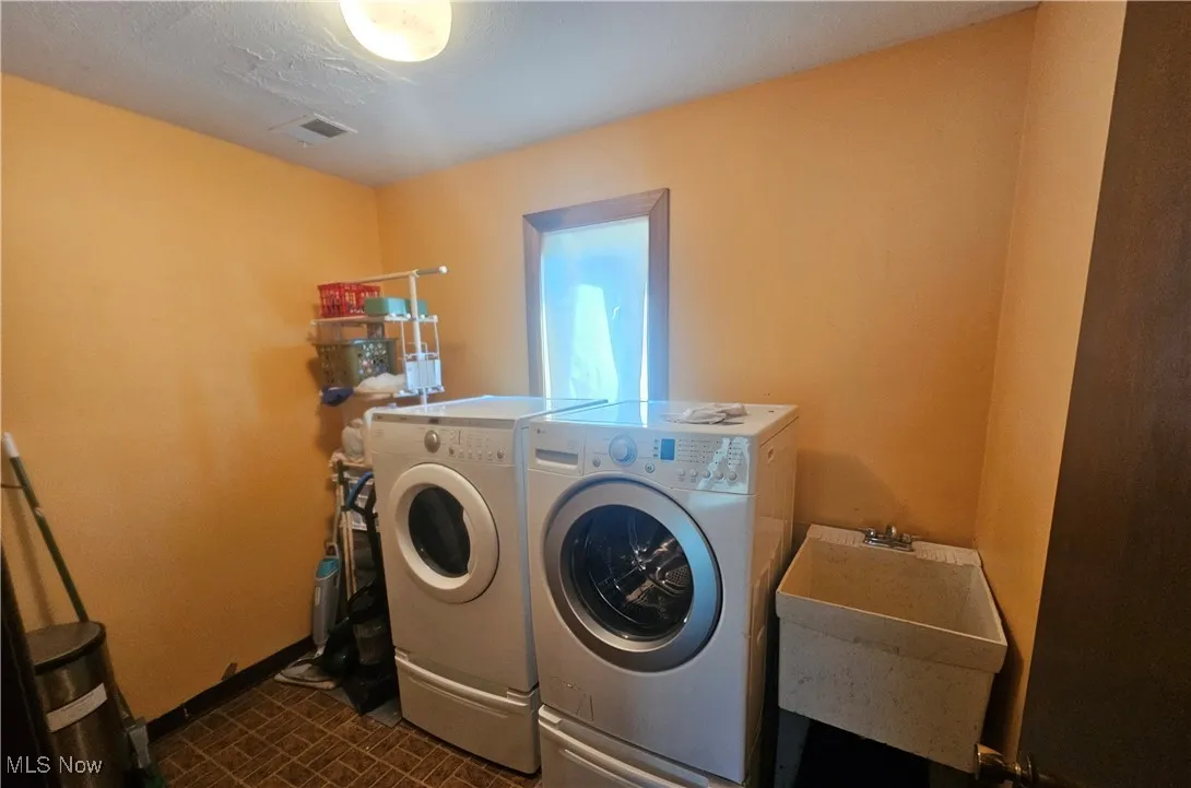 Laundry room with laundry area, visible vents, washing machine and dryer, baseboards, and a sink