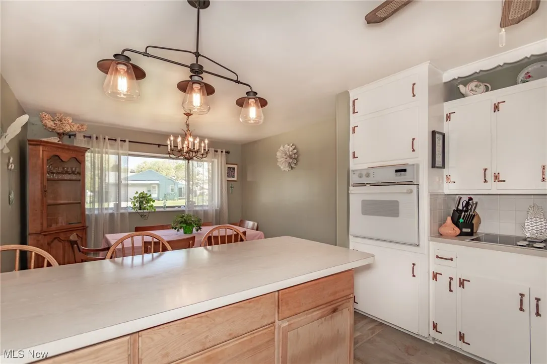 Kitchen with black electric stovetop, light countertops, a chandelier, tasteful backsplash, and white oven