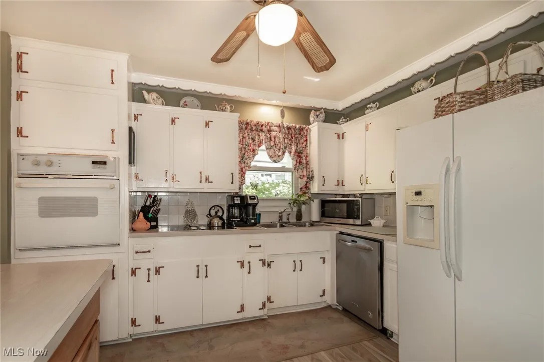 Kitchen featuring a sink, light countertops, white cabinets, a ceiling fan, and appliances with stainless steel finishes