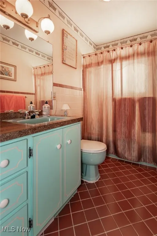 Bathroom with vanity, toilet, tile patterned floors, a wainscoted wall, and tile walls
