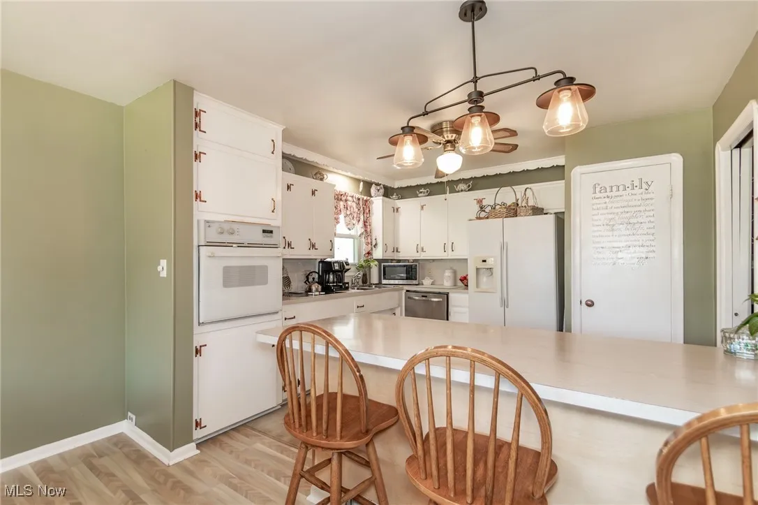 Kitchen with appliances with stainless steel finishes, light wood-style floors, light countertops, white cabinetry, and a kitchen bar