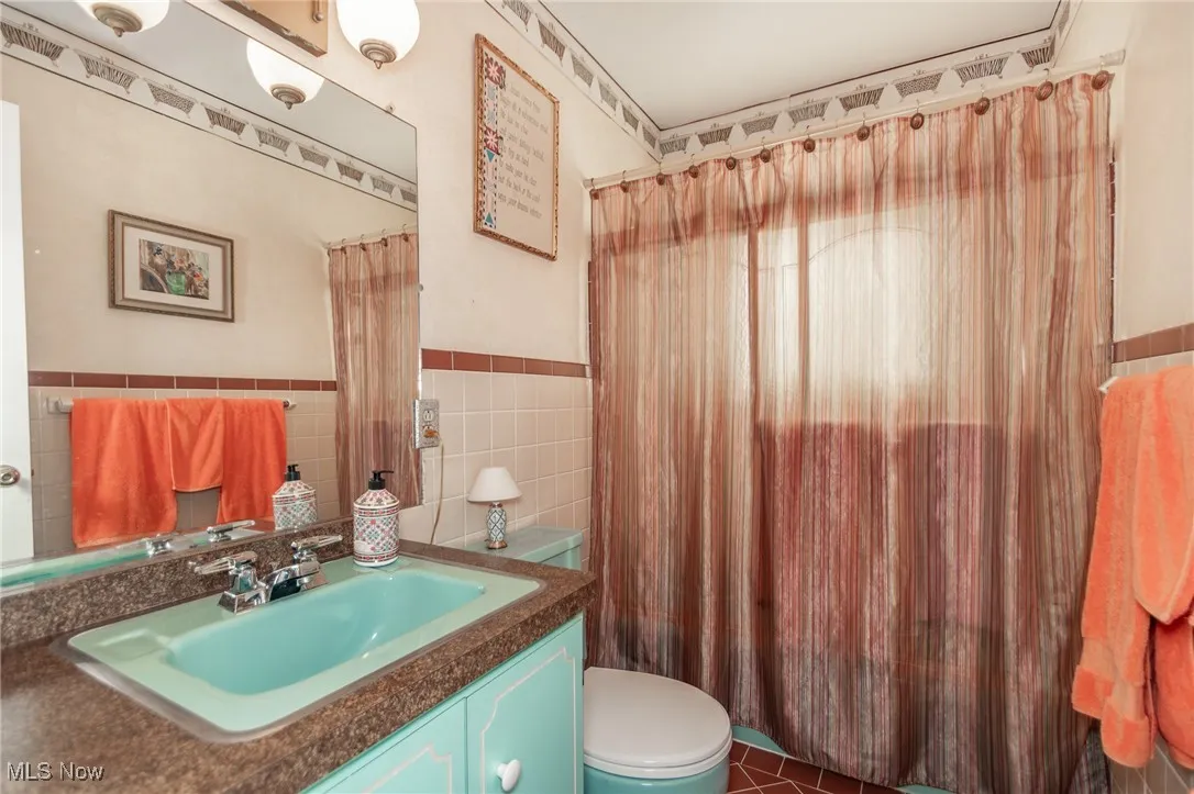 Bathroom with vanity, wainscoting, toilet, and tile walls