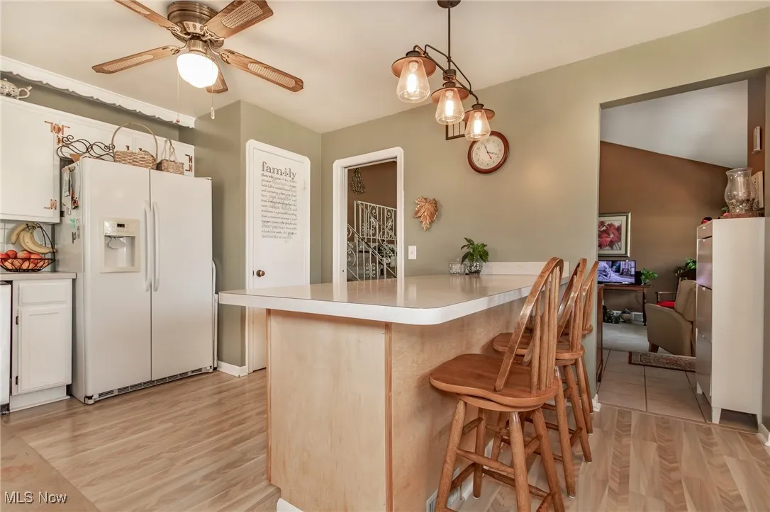 Kitchen with a peninsula, ceiling fan, a kitchen breakfast bar, light wood-type flooring, and white fridge with ice dispenser