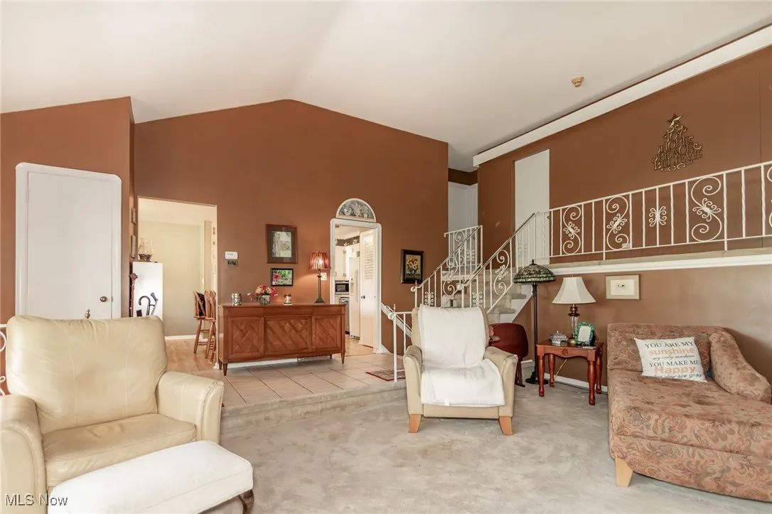 Living area featuring carpet flooring, high vaulted ceiling, and stairway