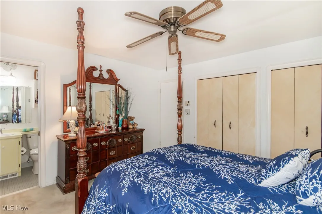 Bedroom with ceiling fan, visible vents, two closets, connected bathroom, and light carpet
