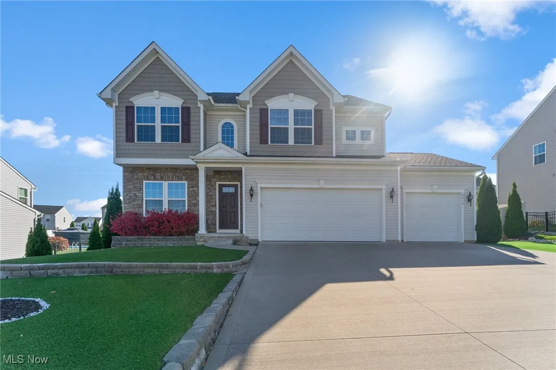 View of front facade with an attached garage, stone siding, driveway, and a front yard