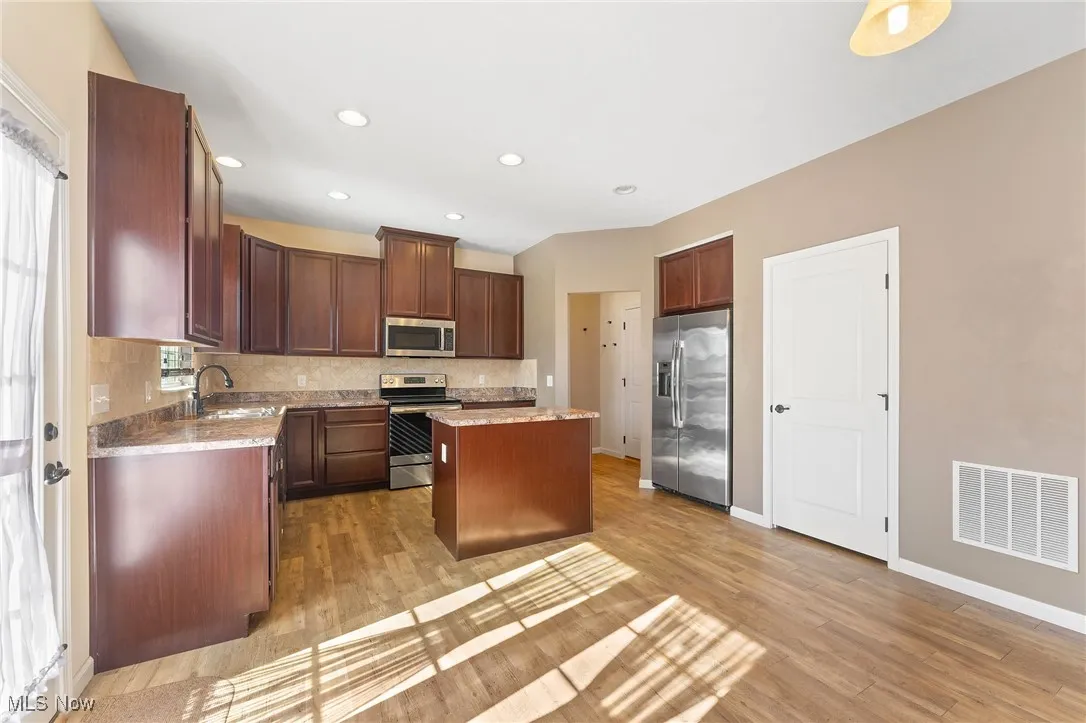 Kitchen with a kitchen island, backsplash, visible vents, appliances with stainless steel finishes, and light wood-type flooring