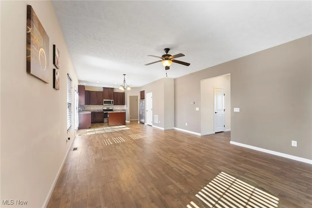 Unfurnished living room featuring baseboards, ceiling fan with notable chandelier, wood finished floors, and visible vents