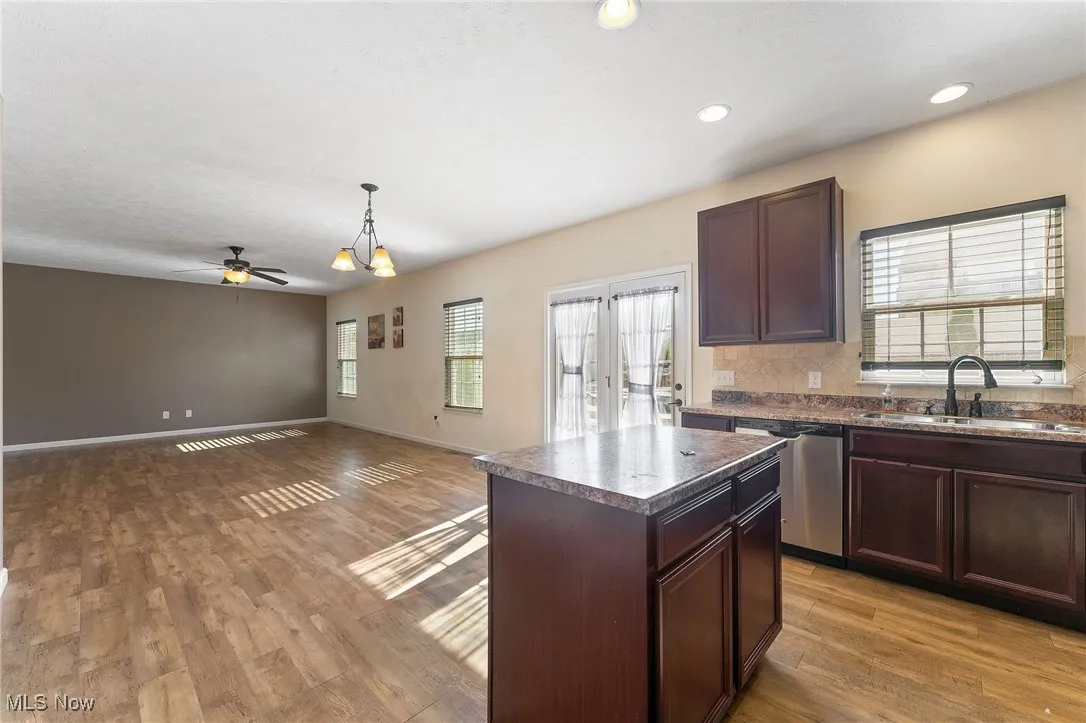 Kitchen featuring dark countertops, a sink, a center island, wood finished floors, and stainless steel dishwasher