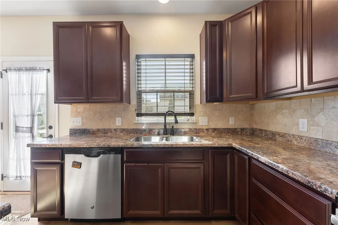 Kitchen with a sink, dark countertops, decorative backsplash, and stainless steel dishwasher