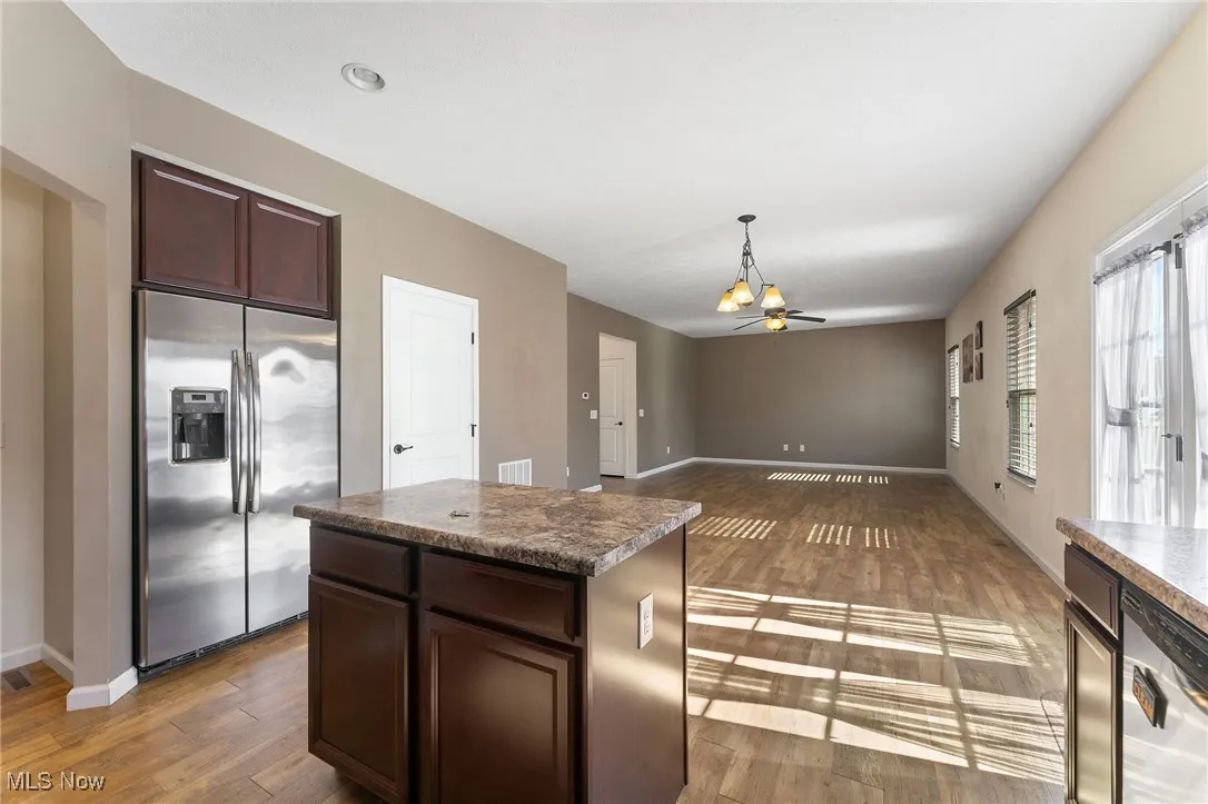 Kitchen featuring a kitchen island, appliances with stainless steel finishes, wood finished floors, dark brown cabinets, and a notable chandelier