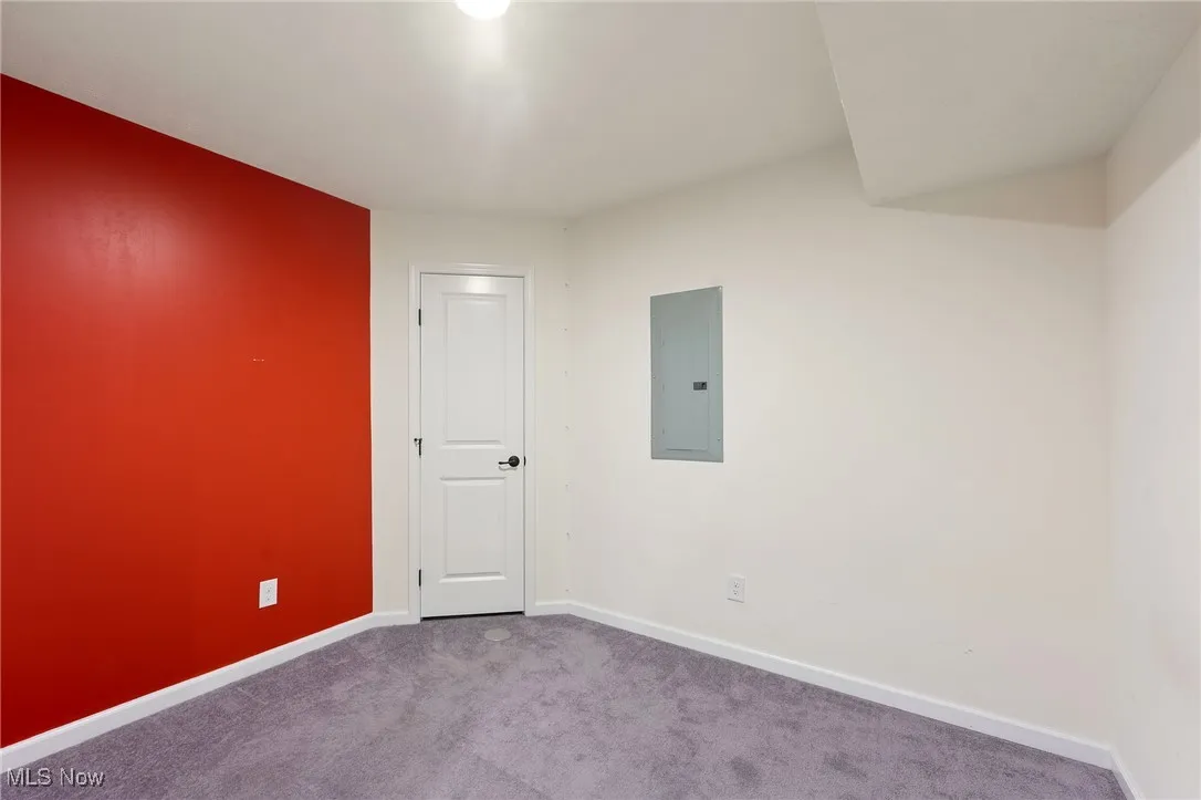 Carpeted spare room featuring baseboards and electric panel