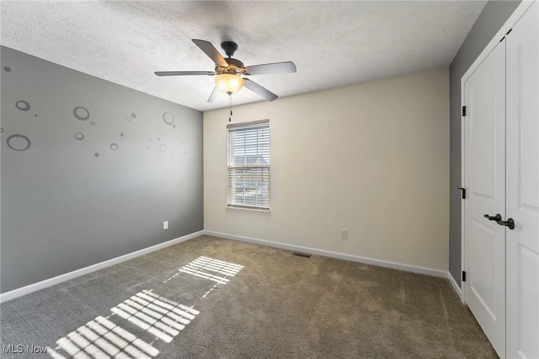 Unfurnished bedroom featuring carpet flooring, a textured ceiling, a ceiling fan, baseboards, and a closet