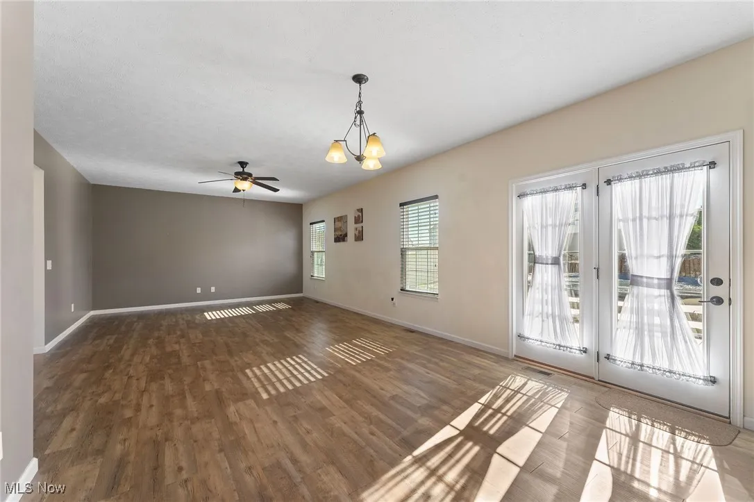 Unfurnished living room featuring baseboards, ceiling fan with notable chandelier, and wood finished floors