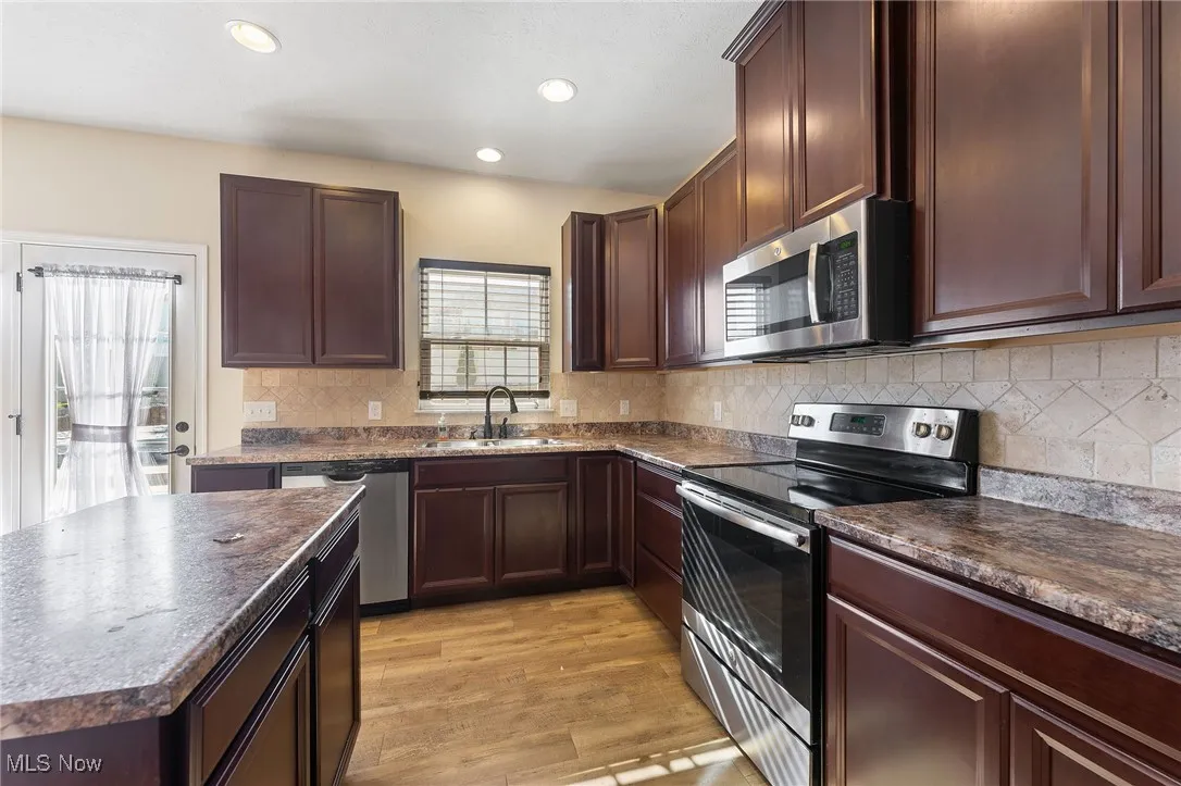 Kitchen with light wood-type flooring, a sink, dark countertops, and stainless steel appliances
