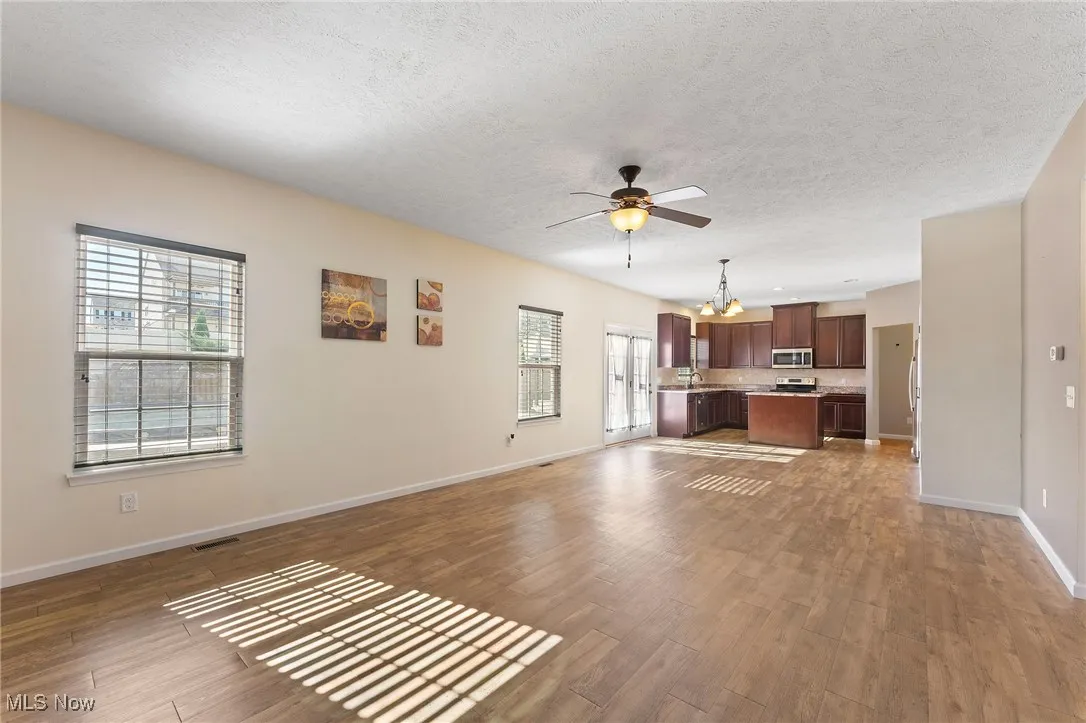 Unfurnished living room featuring visible vents, wood finished floors, baseboards, a textured ceiling, and ceiling fan with notable chandelier