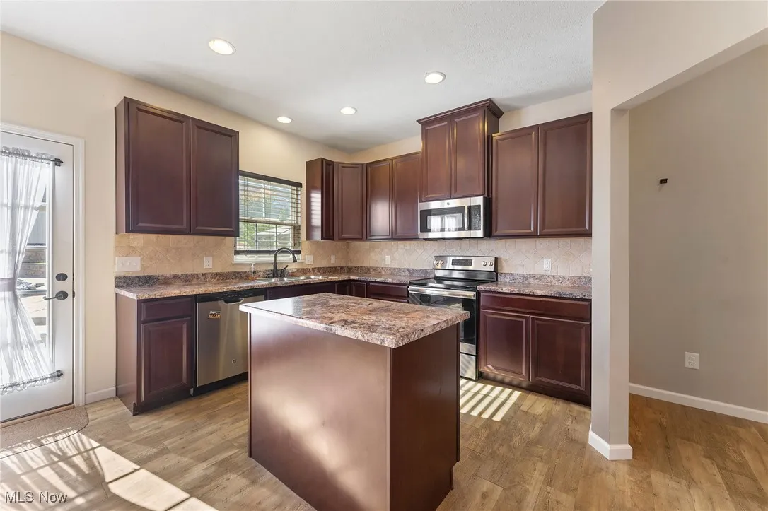 Kitchen with dark brown cabinetry, backsplash, appliances with stainless steel finishes, a sink, and light wood-style flooring