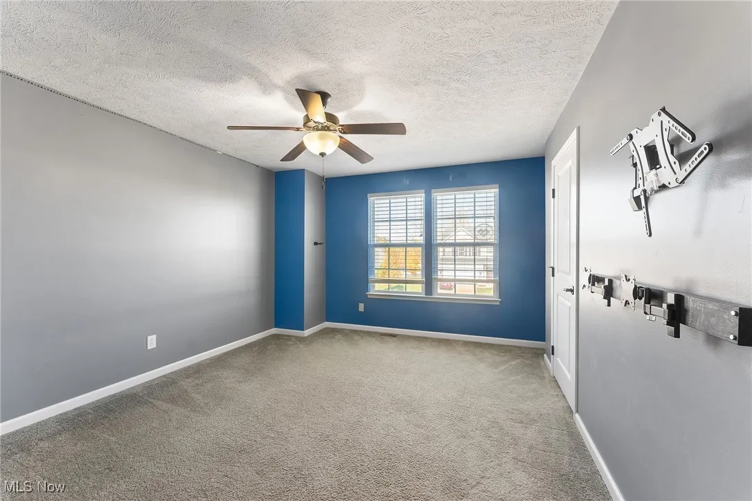Carpeted spare room featuring baseboards, ceiling fan, and a textured ceiling