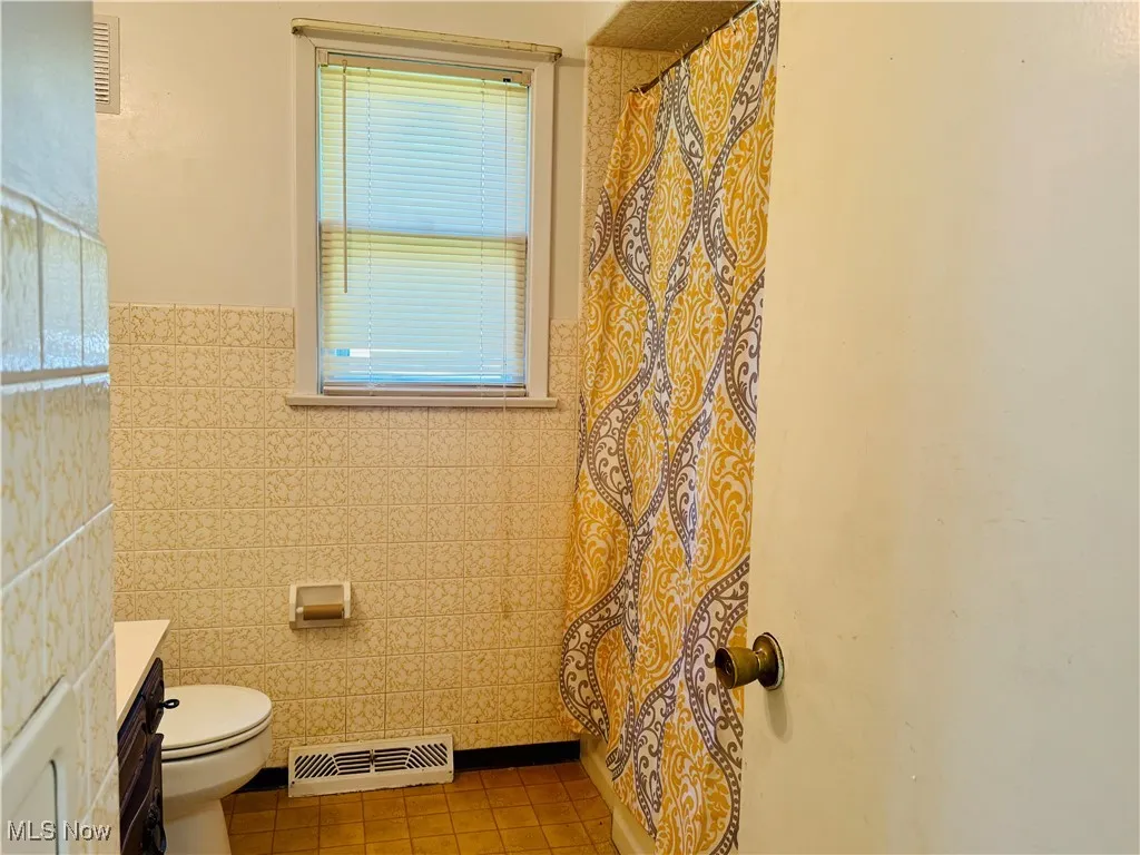 Full bath featuring visible vents, tile patterned flooring, toilet, tile walls, and a wainscoted wall