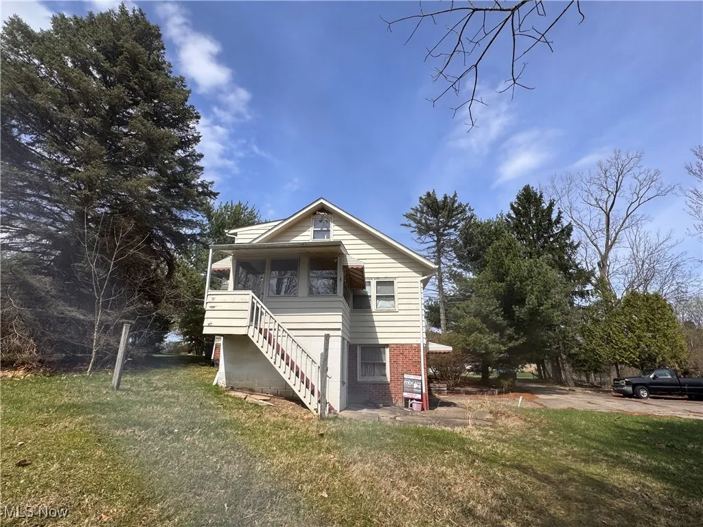 View of back of home with stairs leading to sunroom, and a  back lawn