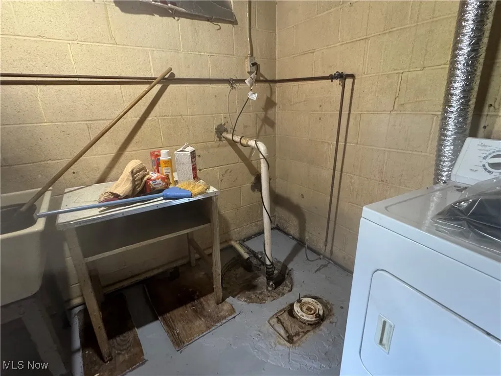 Clothes washing area featuring washer / clothes dryer and concrete block wall and sump pump