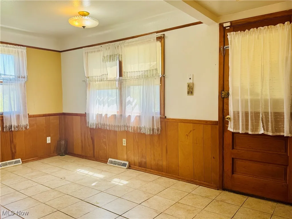 Empty room with wood walls, visible vents, and wainscoting