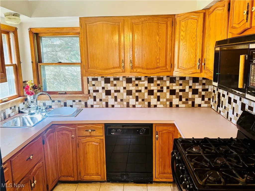 Kitchen featuring light countertops, backsplash, a sink, and black appliances