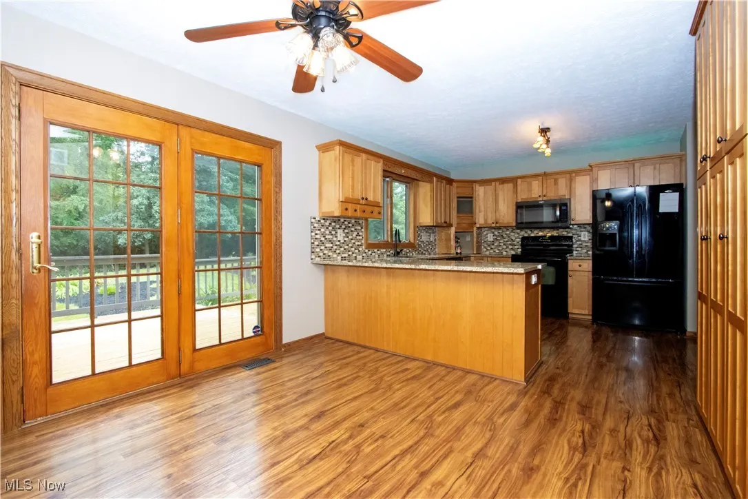 Kitchen with black appliances, a peninsula, backsplash, and dark wood-type flooring