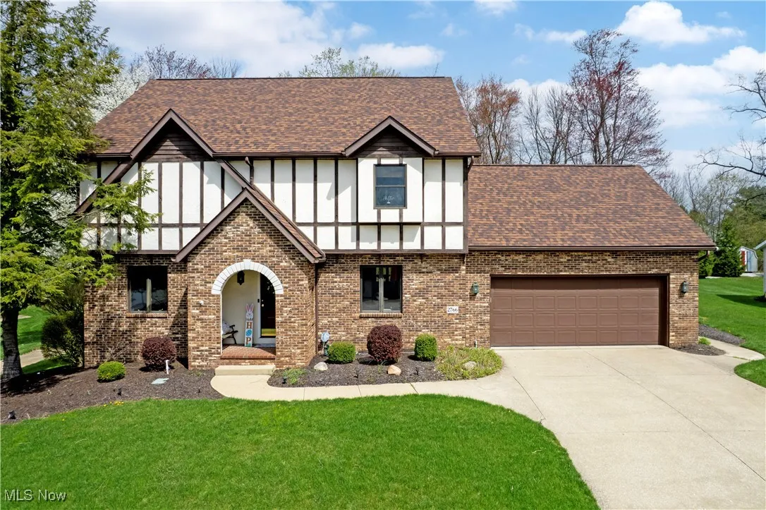 Tudor home with concrete driveway, brick siding, a shingled roof, and a front lawn