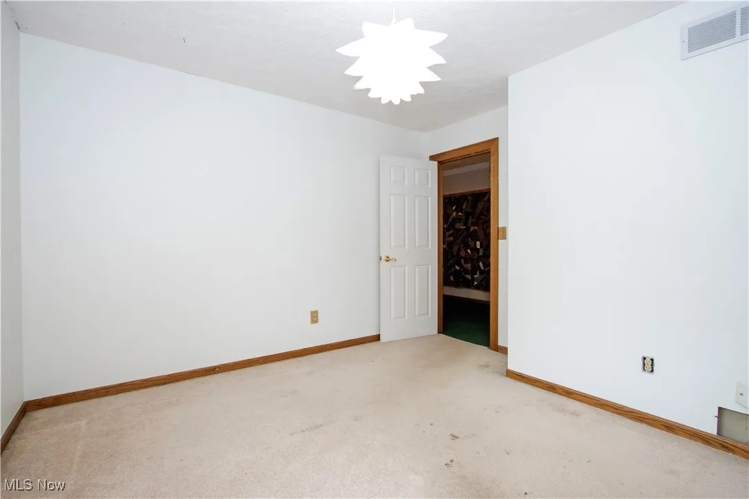Carpeted empty room with baseboards and a chandelier