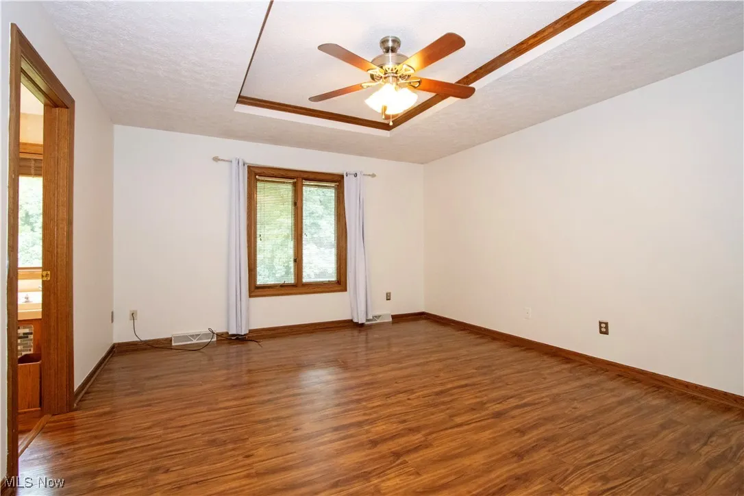 Spare room featuring wood finished floors, a ceiling fan, a tray ceiling, and a textured ceiling