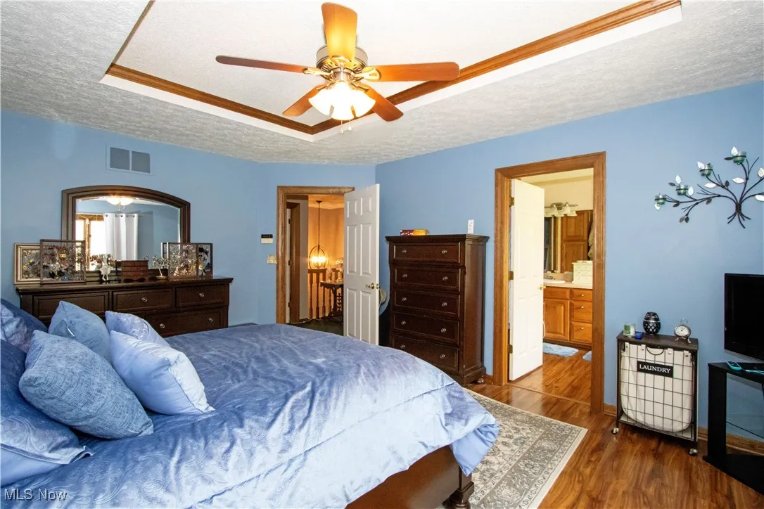 Bedroom featuring ensuite bath, a textured ceiling, wood finished floors, a tray ceiling, and visible vents