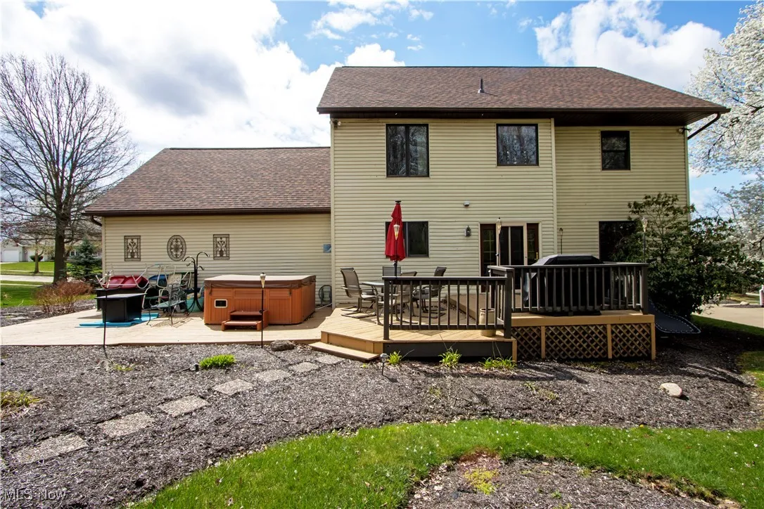 Rear view of property with a hot tub, a wooden deck, a shingled roof, and a patio area