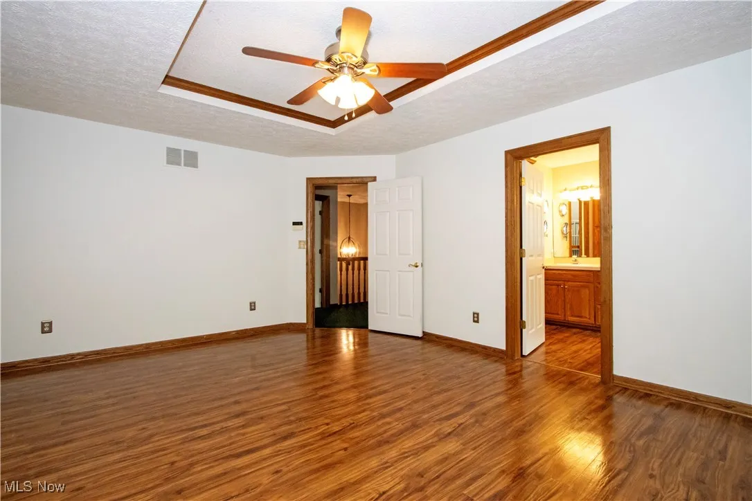 Empty room featuring wood finished floors, a textured ceiling, a ceiling fan, and a tray ceiling