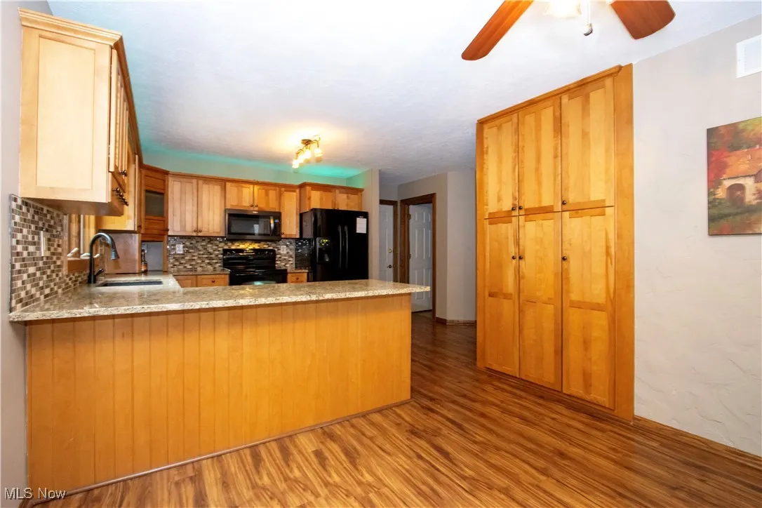 Kitchen featuring black appliances, decorative backsplash, a peninsula, wood finished floors, and a ceiling fan