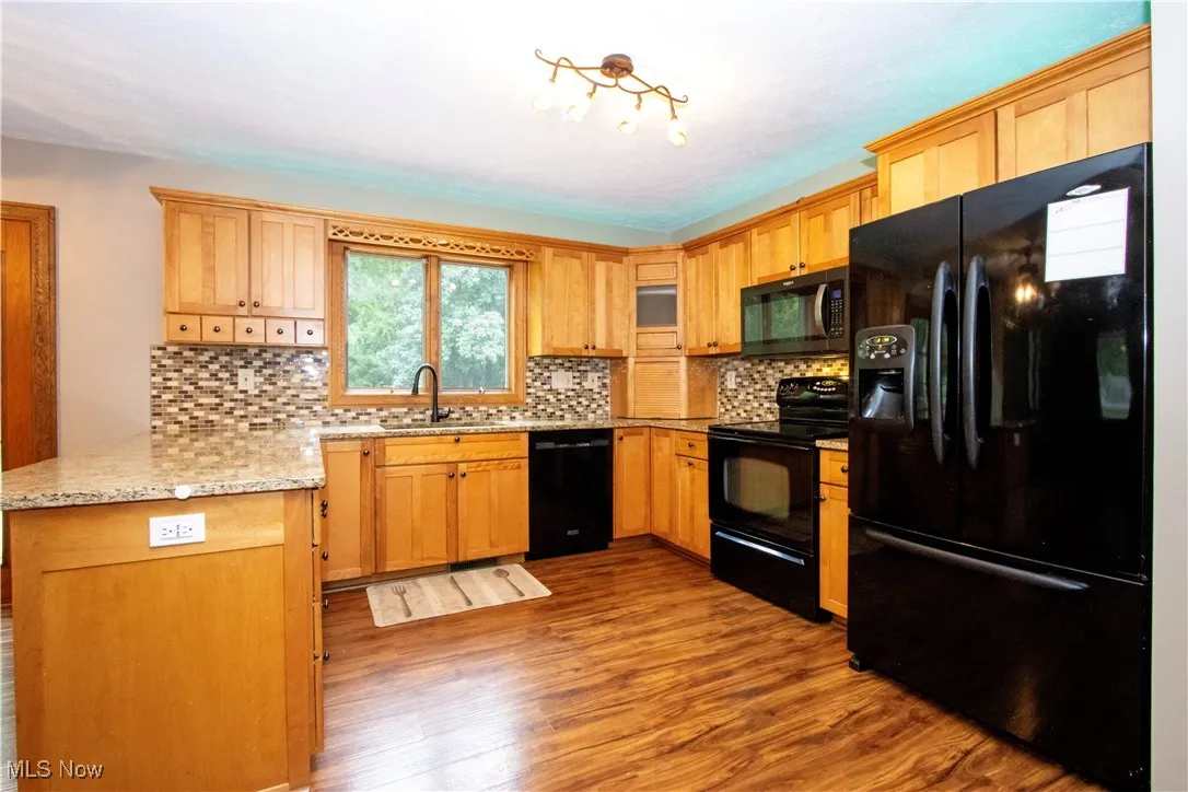 Kitchen featuring black appliances, dark wood-style floors, tasteful backsplash, a peninsula, and light stone countertops