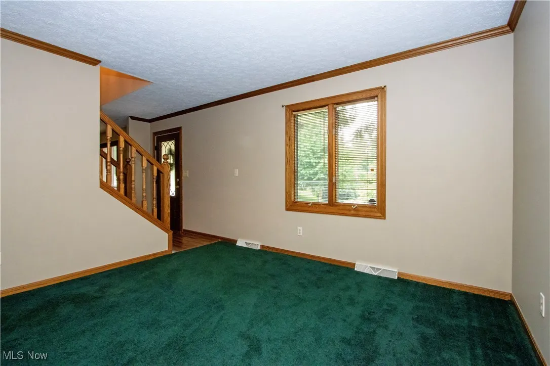 Carpeted spare room featuring stairway, a textured ceiling, and ornamental molding