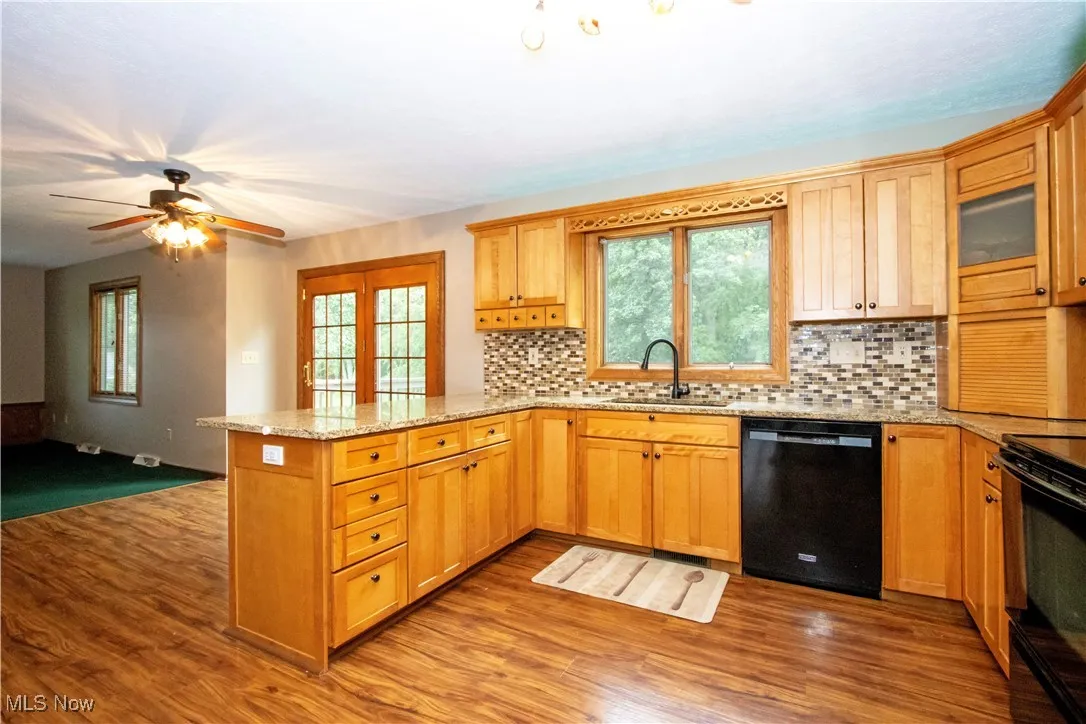 Kitchen with black dishwasher, a peninsula, stove, wood finished floors, and tasteful backsplash